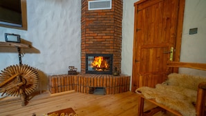 A cozy room with a brick fireplace, wooden furniture, and a fur-covered chair. - Abant Villa Otel (Bolu)