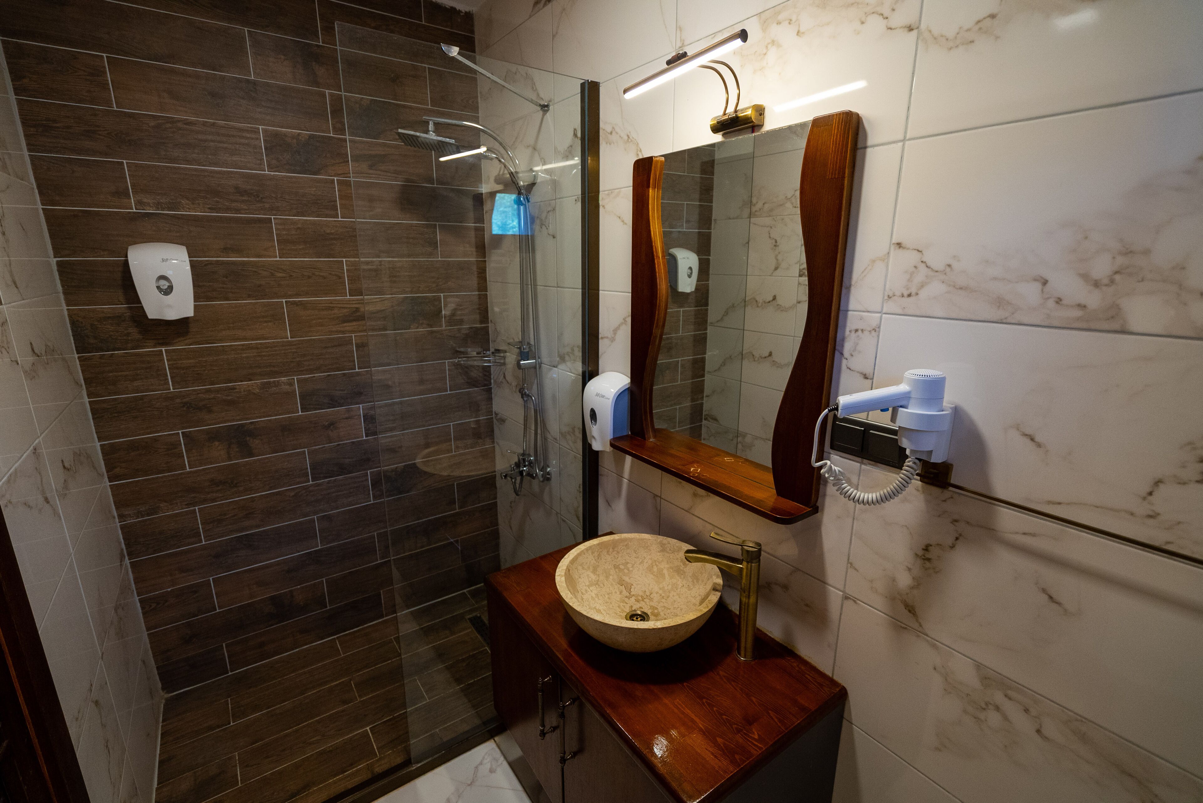 A modern bathroom with a glass-enclosed shower, a marble-tiled wall, a wooden vanity, and a built-in telephone.