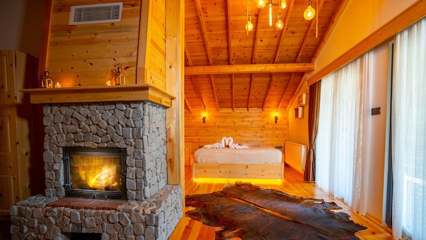 A cozy log cabin room with a stone fireplace, a large fur rug, and a bed with a white headboard. - Abant Villa Otel (Bolu)