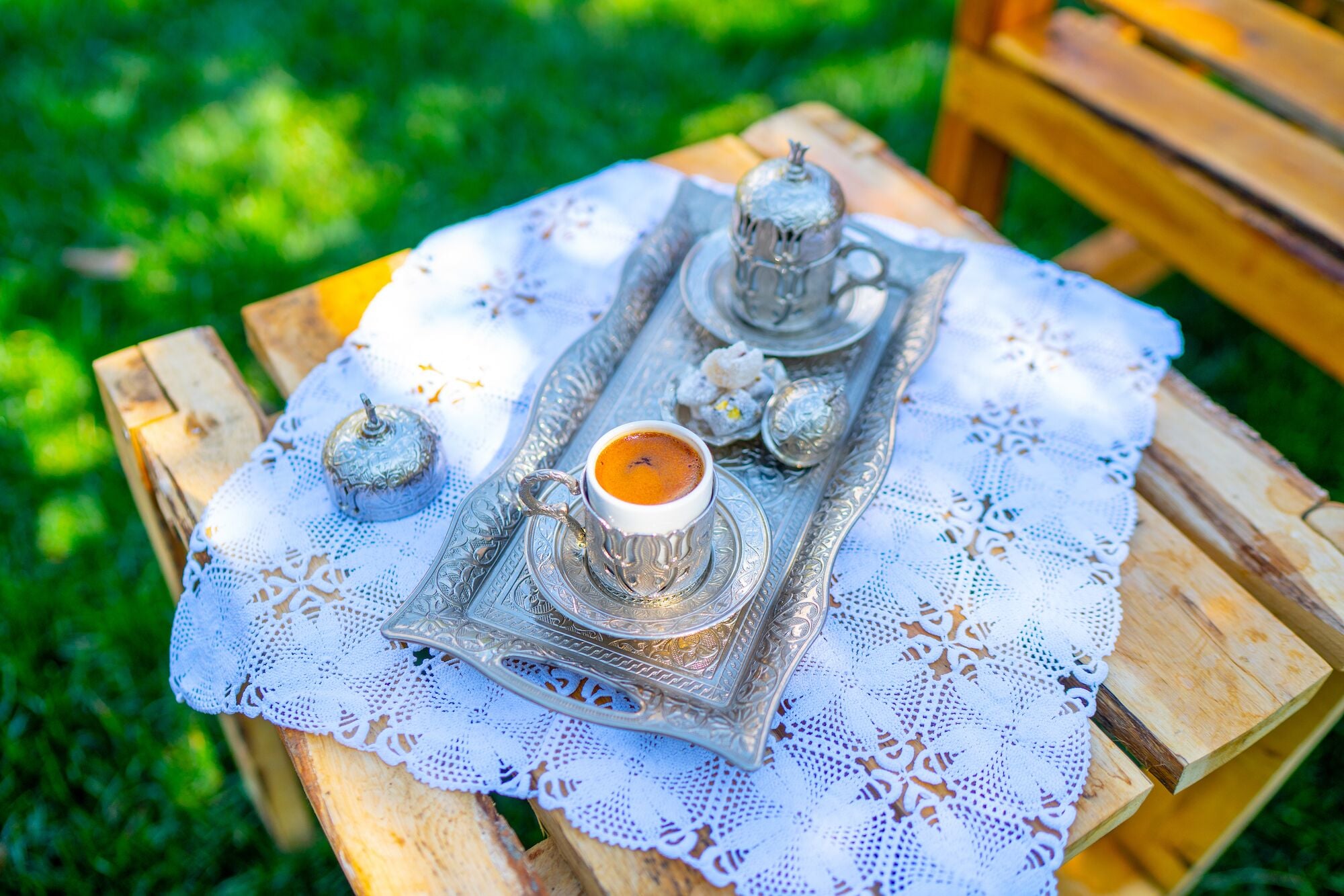 A tray with a cup of coffee, a teapot, and sugar cubes on a lace tablecloth.