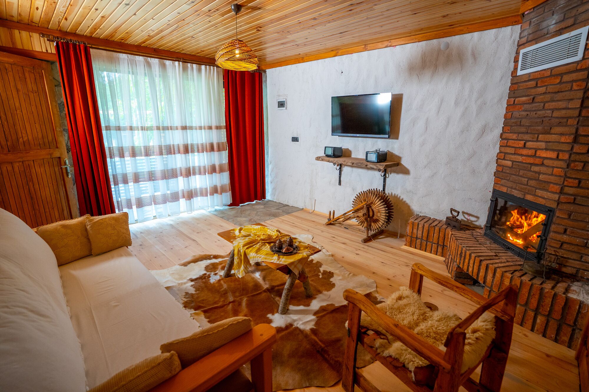 A cozy living room with a fireplace, wooden furniture, a television, and a large window with curtains.