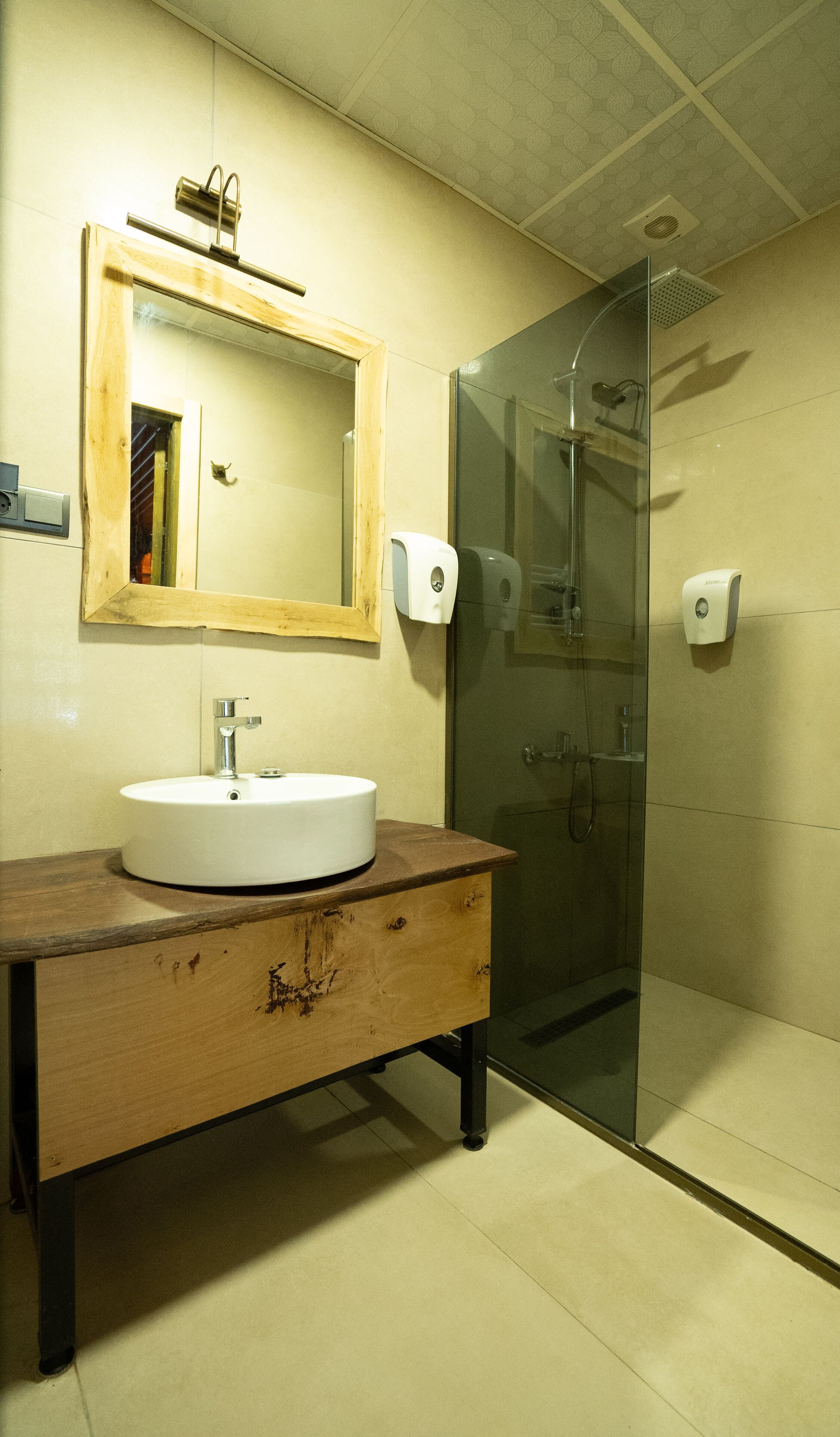 Un baño con tocador de madera, lavamanos blanco, espejo y cabina de ducha de vidrio.