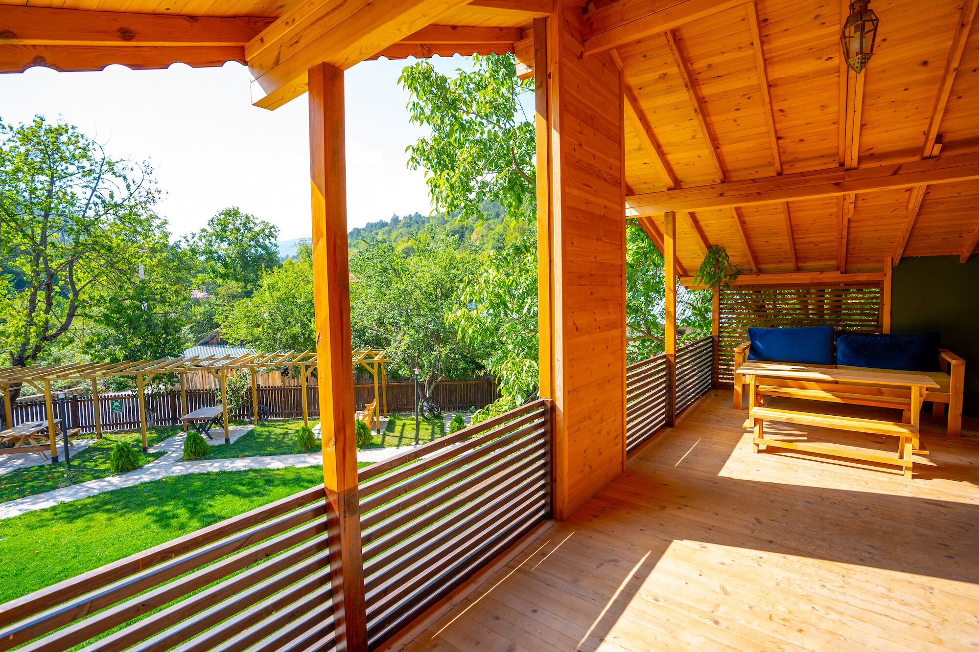 A wooden deck with a bench and a table, overlooking a lush garden and a wooden fence.
