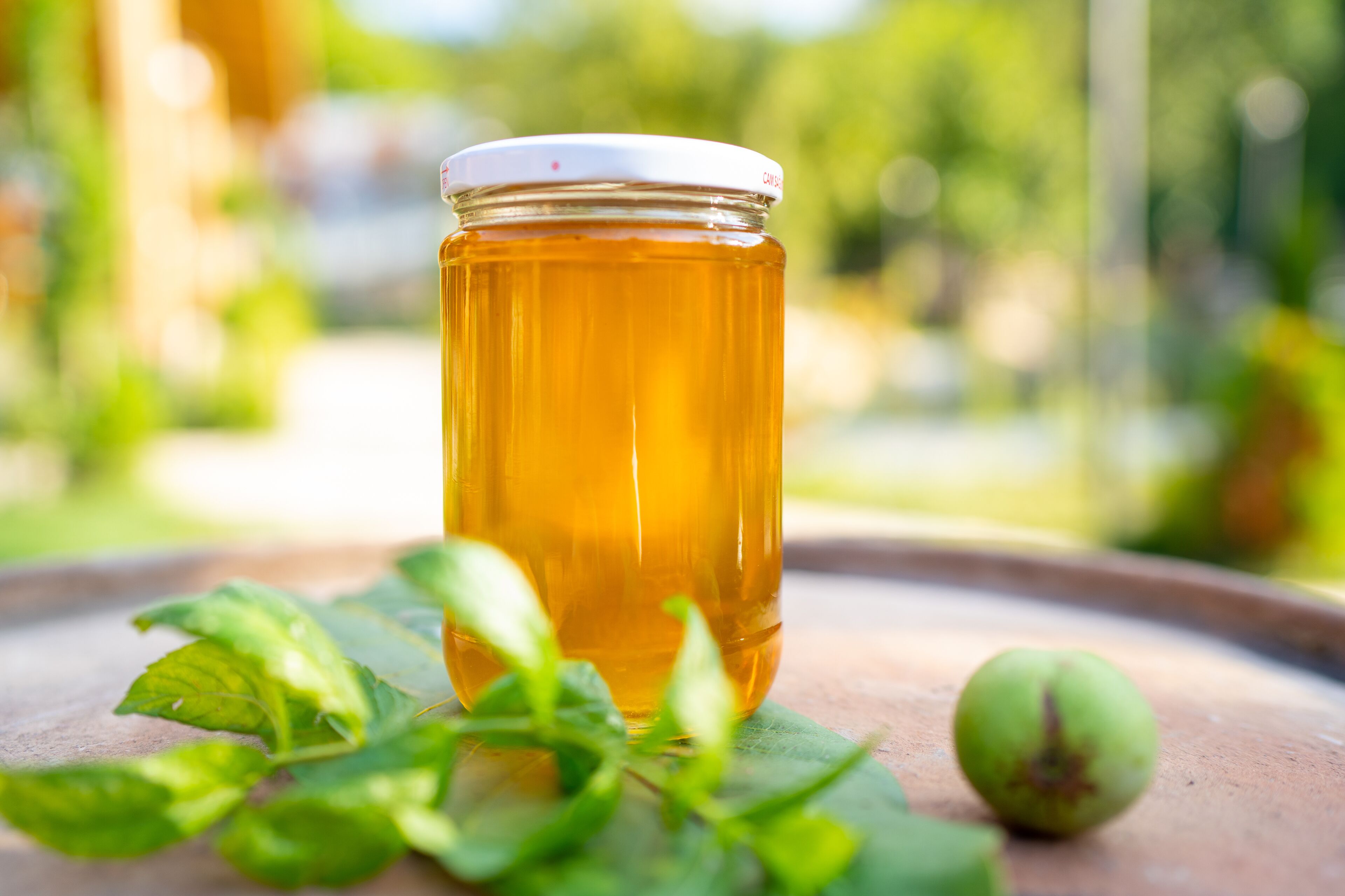 A jar of honey on a ceramic plate with mint leaves and a green fruit.