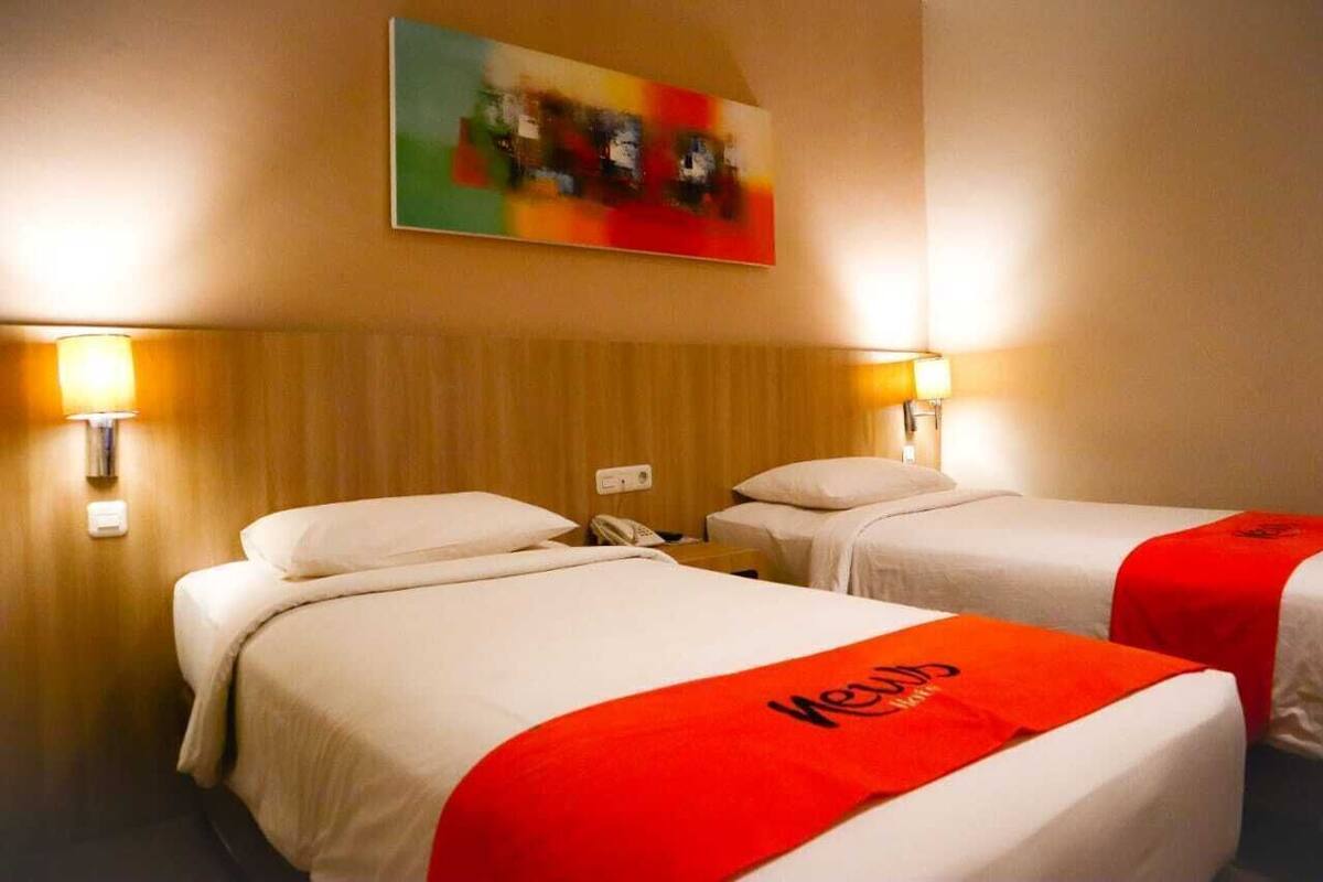 Habitación de hotel con dos camas, cada una con una toalla roja, cabecero de madera y un cuadro sobre las camas.