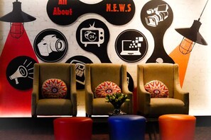 A room with three armchairs, a red and orange lamp, and a wall decorated with circular signs. - News Hotel Surabaya by Graha Pena Jawa Pos (Sidoarjo)