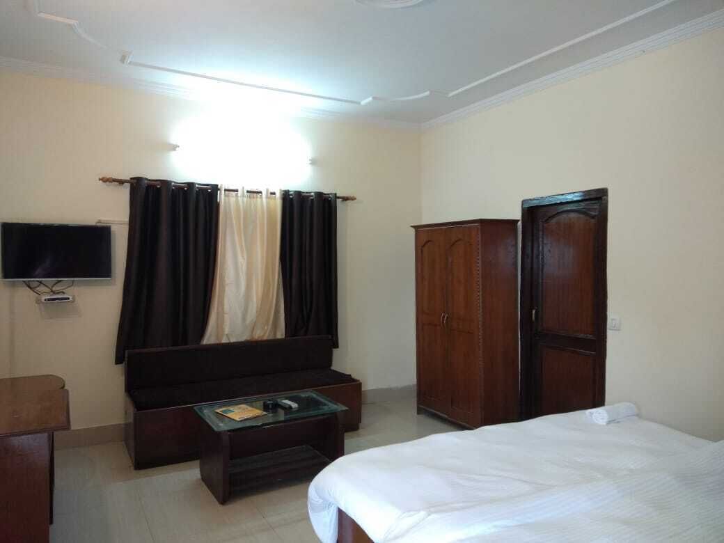 A bedroom with a bed, a wooden wardrobe, a television, a desk, and a window with curtains.