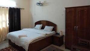 A bedroom with a wooden bed, a nightstand, a wardrobe, and a ceiling fan. - Hotel Killa Niwas (Malvan)