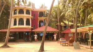A two-story building with a red-tiled roof, surrounded by palm trees. - Hotel Killa Niwas (Malvan)