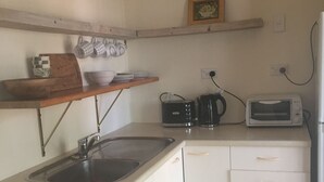 Una cocina compacta con lavavajillas Bosch, microondas, tetera y tostadora. Hay un estante de madera sobre el fregadero y un pequeño cuadro en la pared.