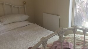 Una cama bien hecha con edredón estampado de flores, un cabecero blanco y una ventana con vistas a los árboles.