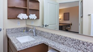 A bathroom with a granite countertop, a white sink, and a mirror reflecting a door and a chair. - Candlewood Suites Louisville - NE Downtown Area by IHG (Louisville)