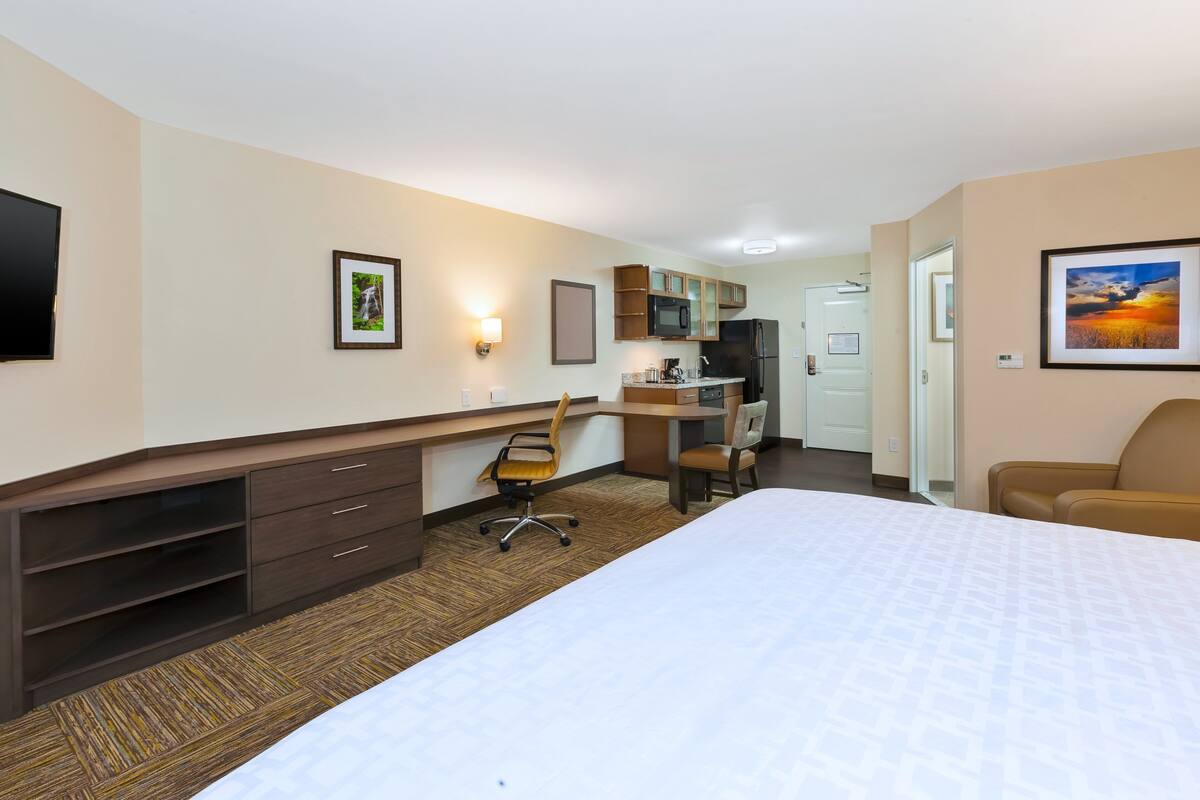 Une chambre d’hôtel équipée d’un lit, d’un bureau, d’une chaise, d’une kitchenette et d’un téléviseur.
