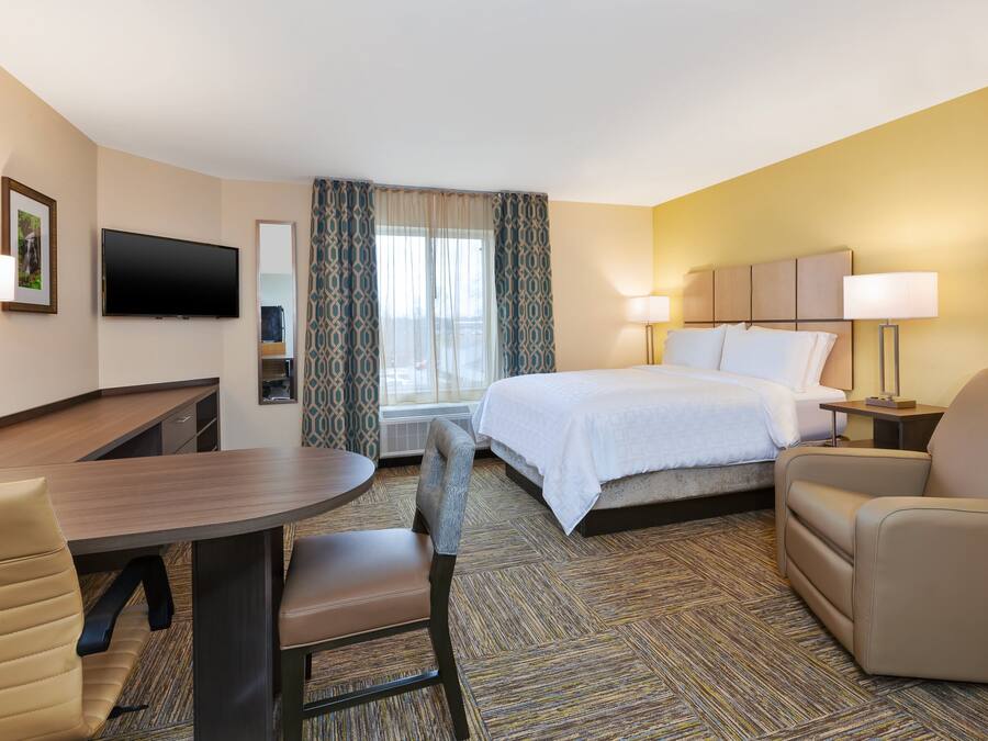 A hotel room with a bed, a desk, a chair, a TV, and a window with curtains.