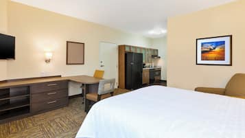 Habitación de hotel con cama, escritorio, silla, televisor y zona de cocina.
