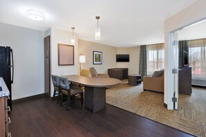 A modern hotel room with a dining area, a sofa, a TV, and a large window.