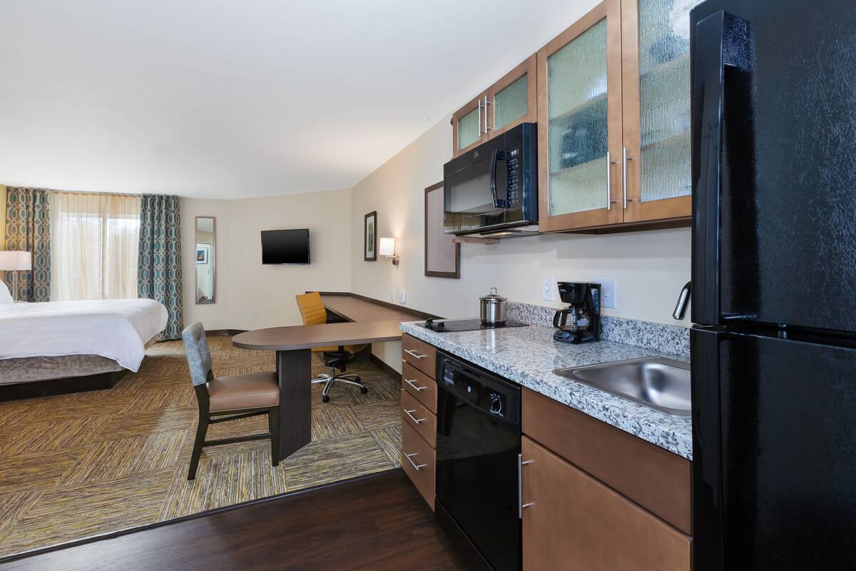 Une chambre d’hôtel équipée d’un lit, d’un bureau, d’une chaise, d’un four à micro-ondes, d’un réfrigérateur, d’un lavabo et d’une télévision.