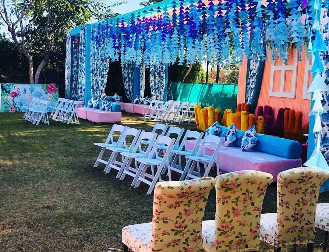 An outdoor event space with white chairs and tables, decorated with hanging paper decorations and colorful cushions.