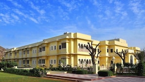 A multi-story building with a yellow facade, arched windows, and a garden in front. - Hotel Raj Bagh Palace (Amer)
