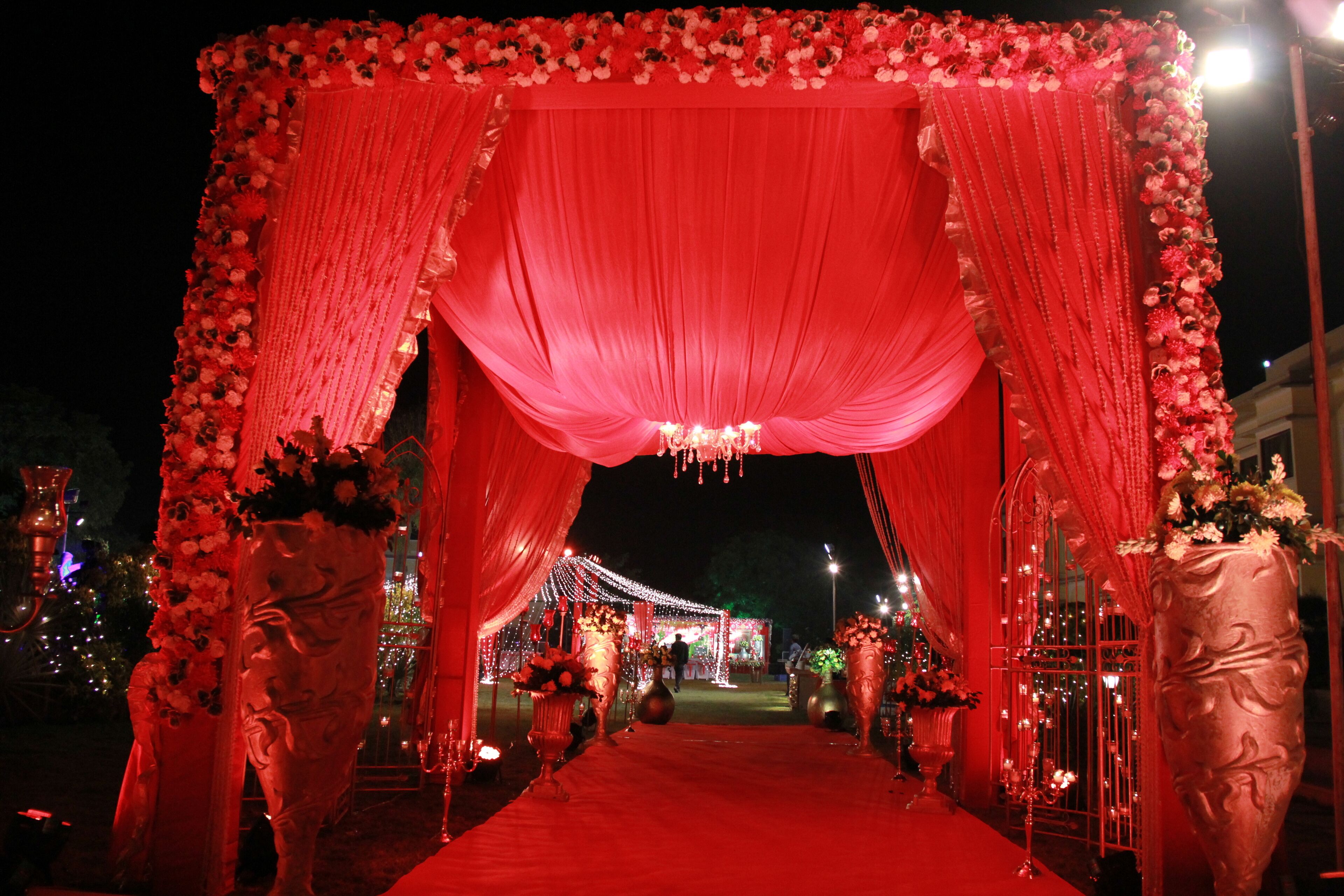 An ornate red archway with draped fabric and floral decorations, leading to a well-lit pathway.