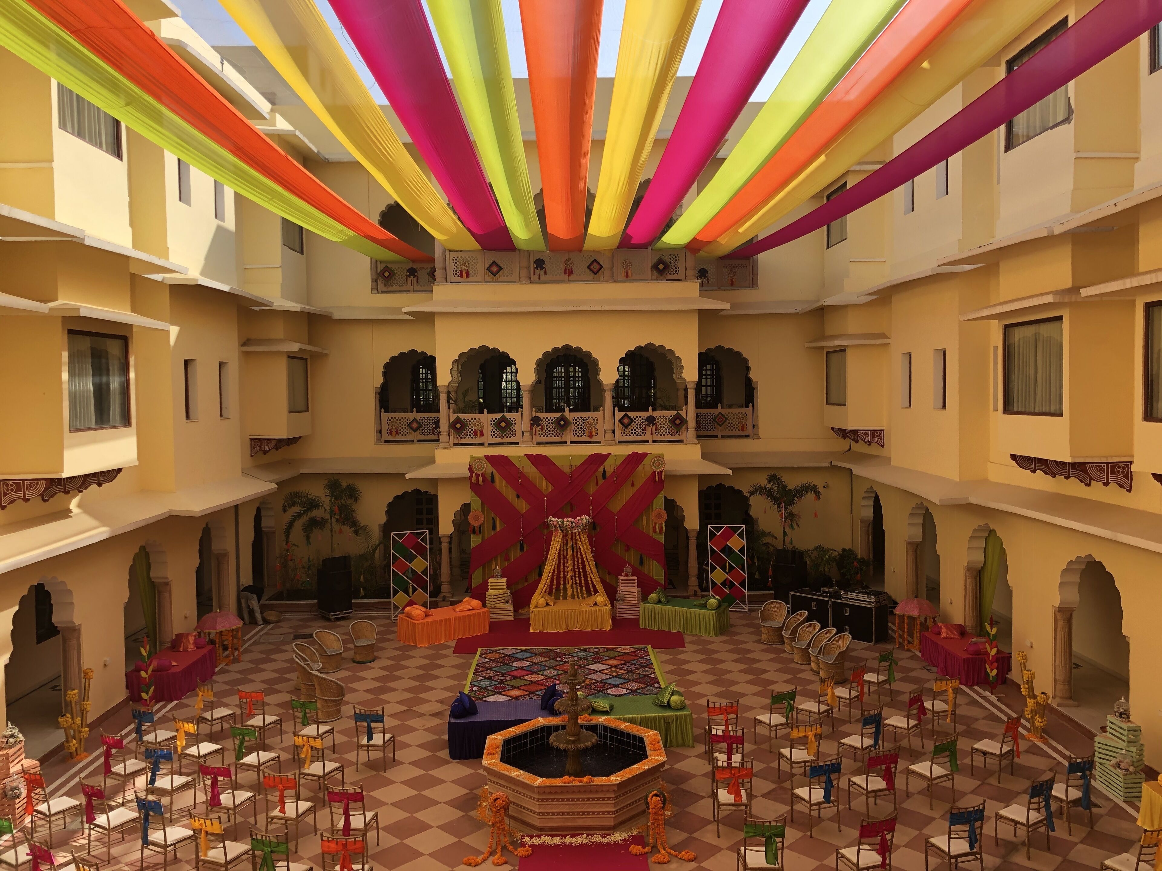 Un amplio patio con un escenario central, varias zonas de estar y una fuente decorativa.