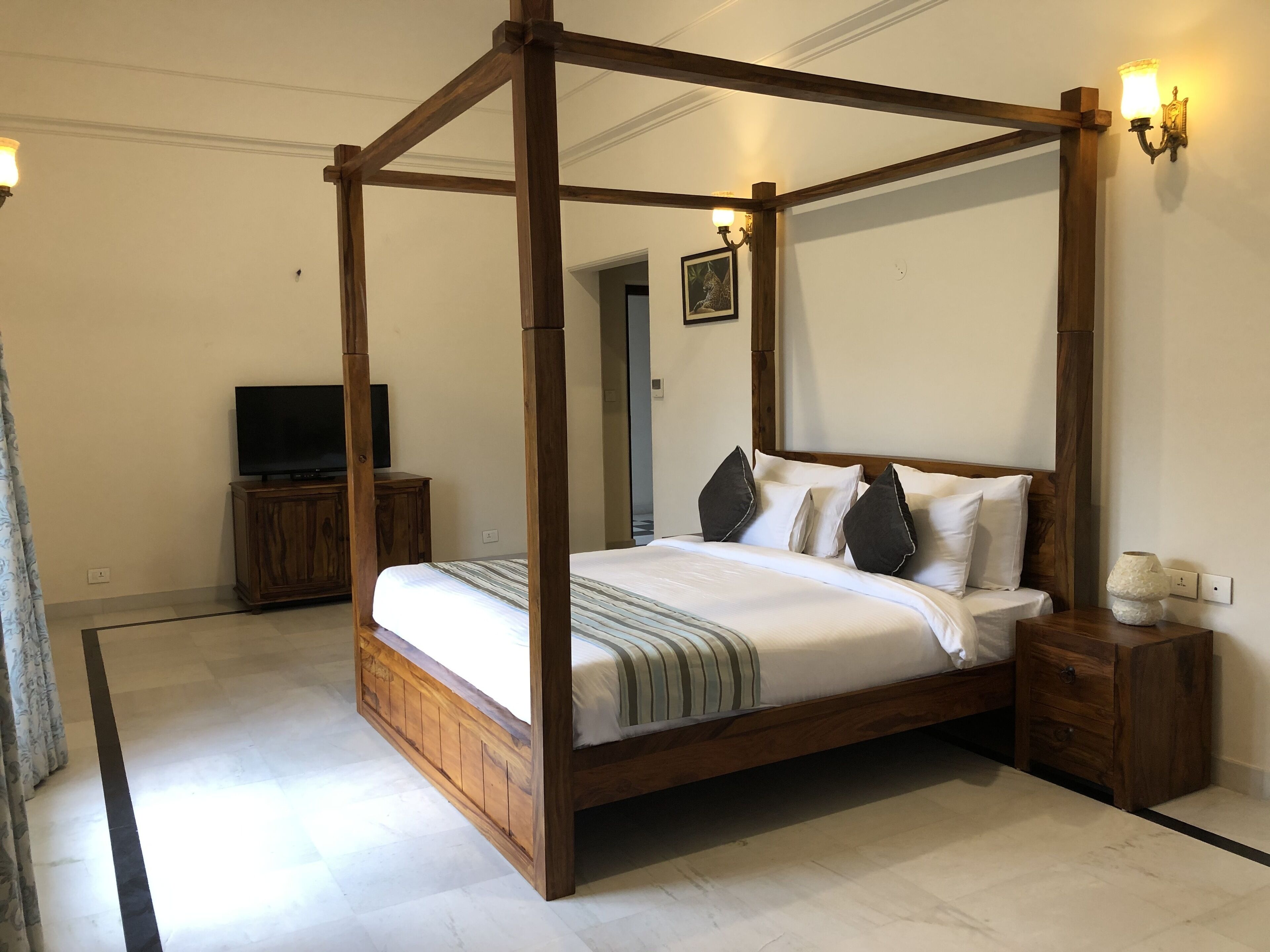 Una cama con dosel de madera, un televisor sobre un mueble de madera y una mesita de noche con una lámpara.