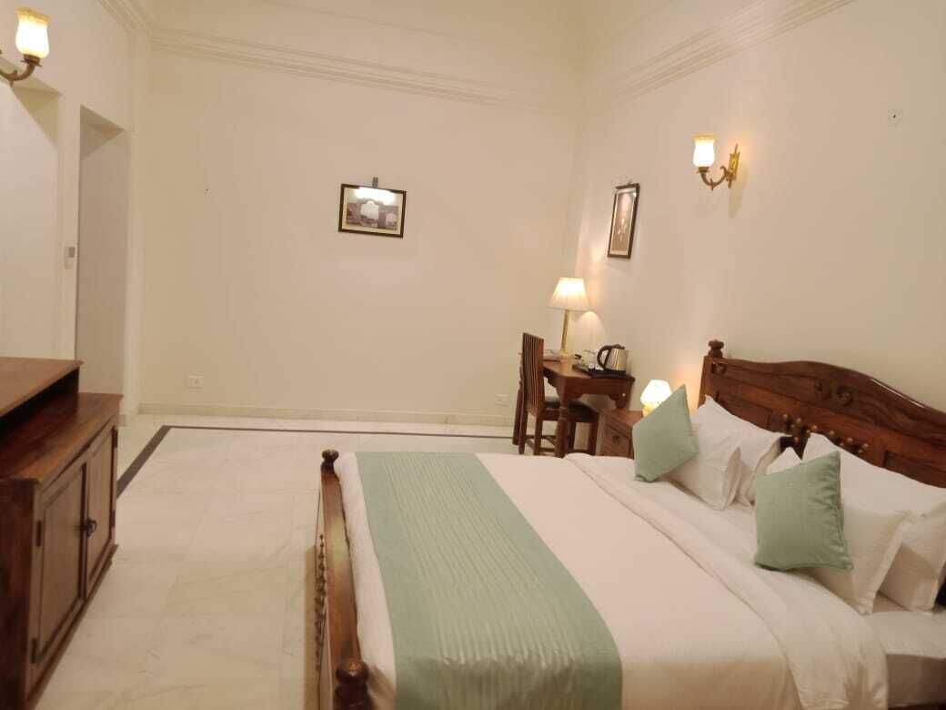 Une chambre d’hôtel avec un grand lit, une tête de lit en bois, un bureau avec une chaise, une lampe et un tableau au mur.