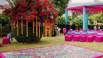Un jardín con un tapete decorativo grande, un pabellón y una zona de estar con sillas rosas.