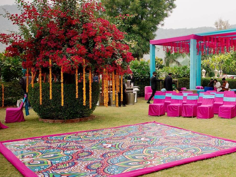 Un jardín con un tapete decorativo grande, un pabellón y una zona de estar con sillas rosas.