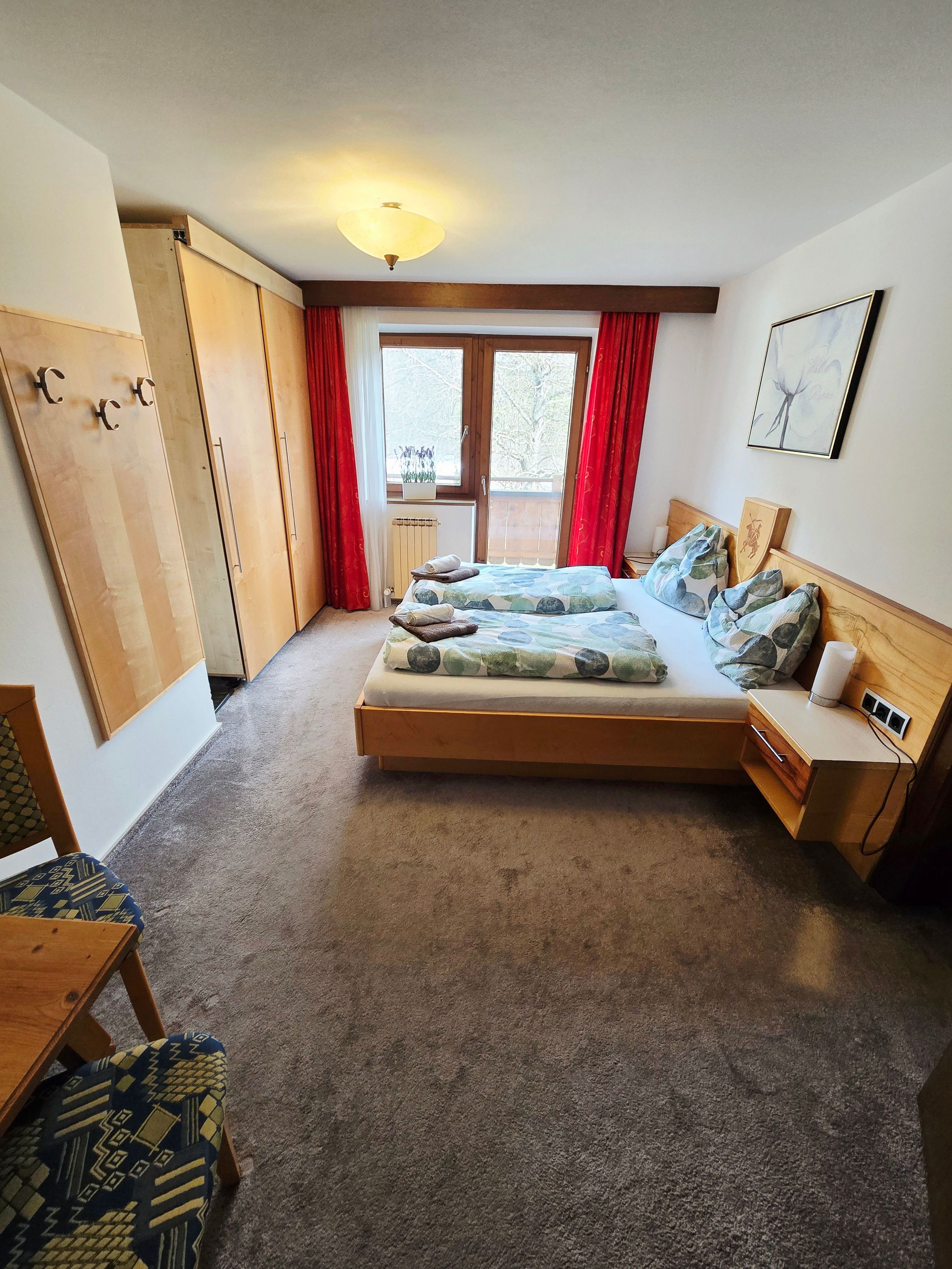 Une chambre à coucher avec un lit, un bureau, une chaise, un radiateur et une fenêtre avec des rideaux.