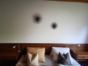 A hotel room with a bed, two wall decorations, and a nightstand with a lamp.