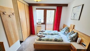 A bedroom with a bed, a desk, a chair, a radiator, and a window with curtains.
