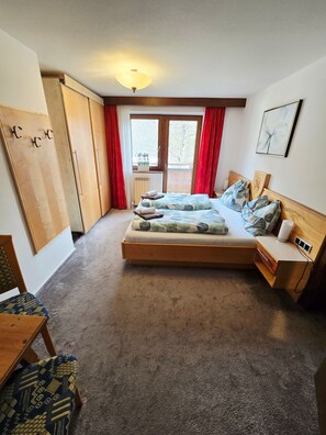 A bedroom with a bed, a desk, a chair, a radiator, and a window with curtains.