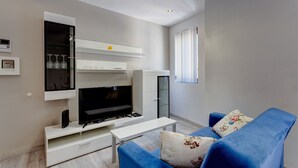 A modern living room with a flat-screen TV, white shelving, and a blue sofa. - Idyllic Apartment Just off the Promenade (Sliema)