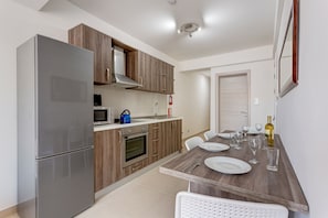 A modern kitchen with a built-in oven, microwave, and kettle, wooden cabinets, and a dining area with a table set for two. - Idyllic 1 Bedroom Apartment in Malta (Msida)