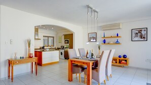 Eine moderne Küche mit Kochinsel, ein Essbereich mit Holztisch und Stühlen sowie ein Wohnbereich mit Sofa und Couchtisch.