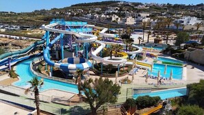Un parque acuático con múltiples toboganes y piscinas, rodeado de palmeras y un paisaje montañoso al fondo.