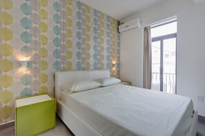 Een slaapkamer met een bed, groene nachtkastjes, behang met een patroon, een airconditioner en een raam met uitzicht.