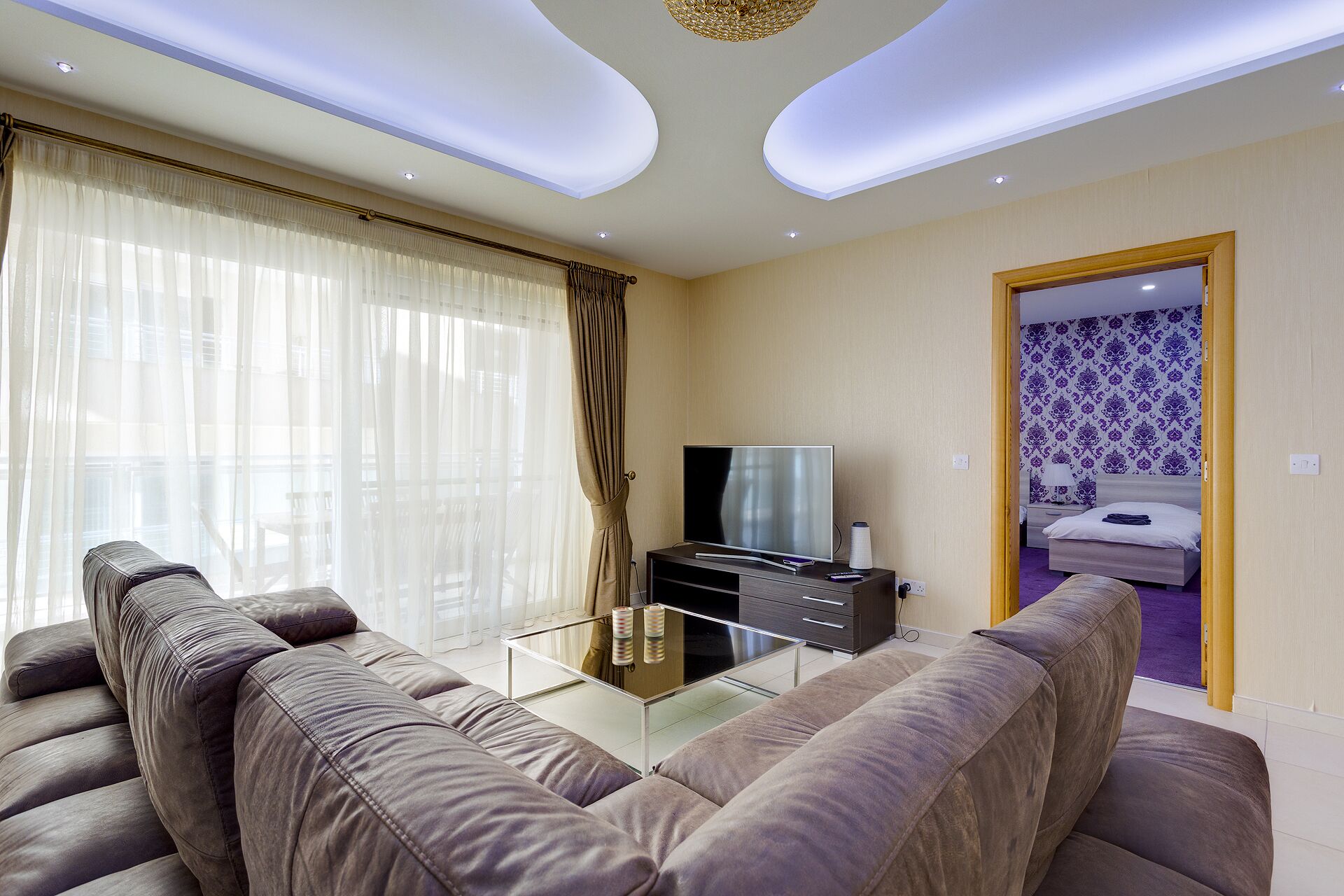 A modern living room with a sofa, a TV, and a glass coffee table.