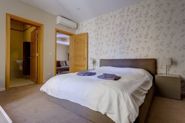 A bedroom with a bed, a nightstand, a lamp, and a bathroom visible through an open door. - Luxury Apt with Side Sea Views & Pool, Top Location (Sliema)
