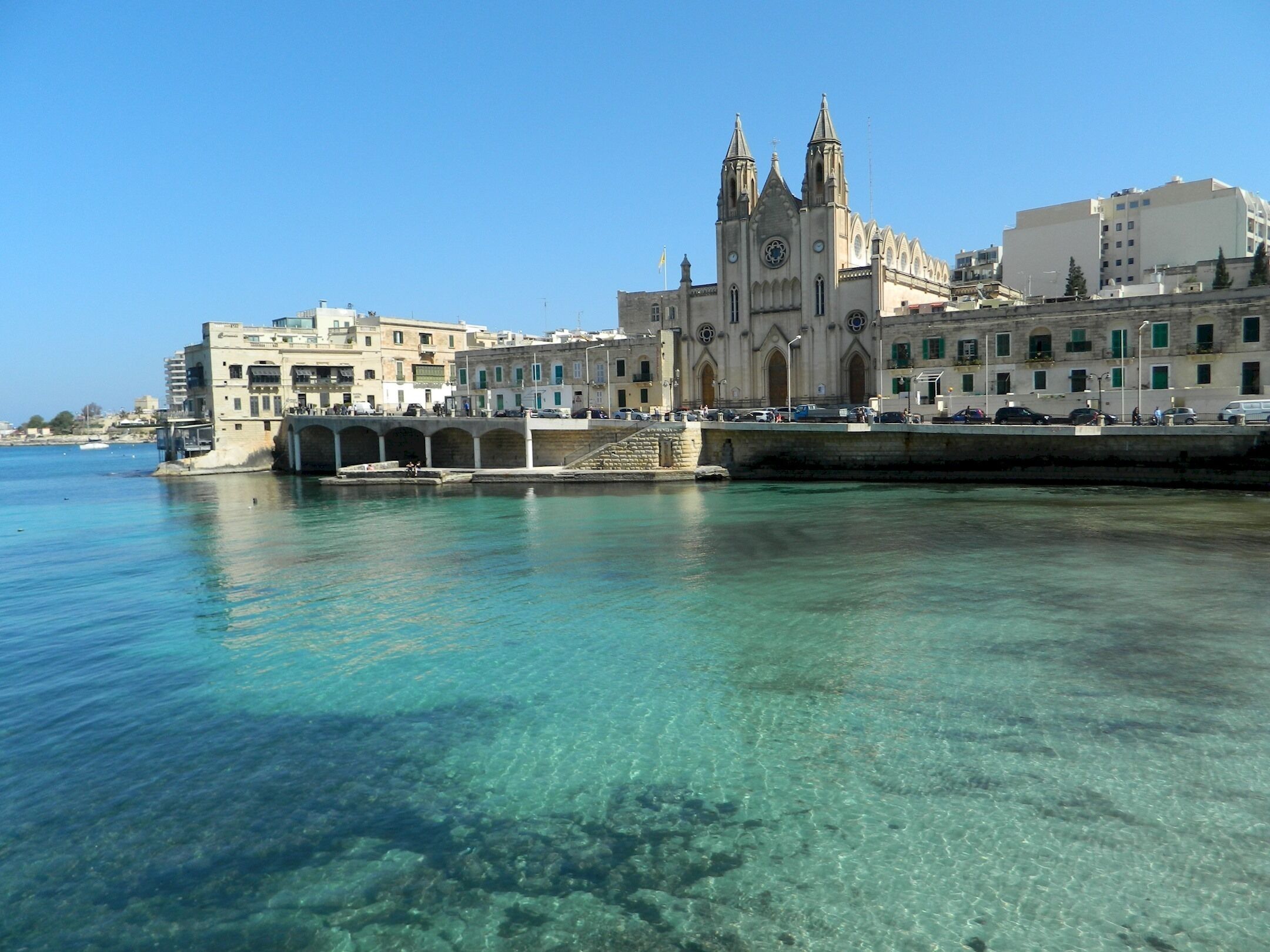 A waterfront cityscape with a prominent cathedral and a bridge.