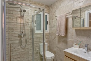 Une salle de bain avec une douche à parois de verre, des toilettes, un lavabo avec un miroir et un porte-serviettes.
