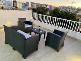 A balcony with wicker furniture, a table, and a bottle of wine.