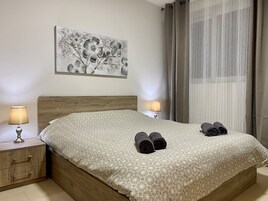 A neatly made bed with a geometric patterned bedspread, two bedside lamps, a wooden nightstand with drawers, and a large abstract floral artwork on the wall.