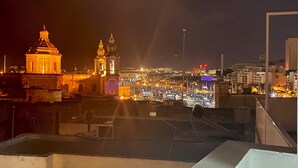 A nighttime cityscape with illuminated buildings and a prominent church tower.