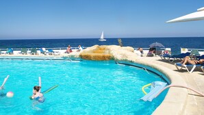 A pool area with lounge chairs and a view of the sea.