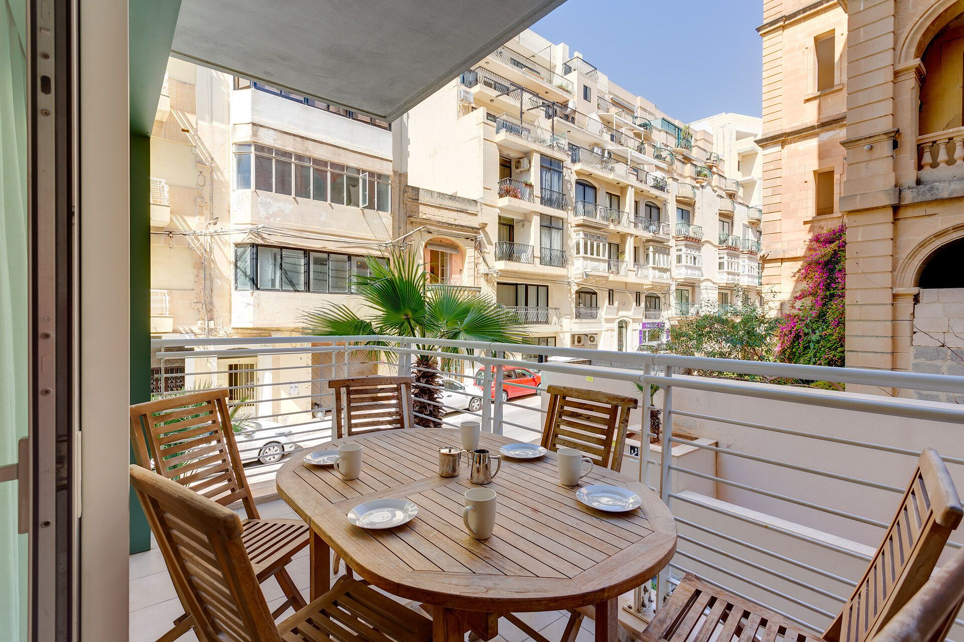 Un balcón con una mesa y sillas de madera, con vistas a una zona residencial con edificios de varios pisos.