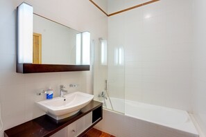 A bathroom with a white sink, a mirror, a wooden vanity, and a bathtub. - Superb Apartment IN Fort Cambridge With Pool (Sliema)