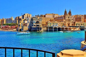 Un paysage urbain côtier avec une église imposante, un pont et des bateaux sur l’eau.
