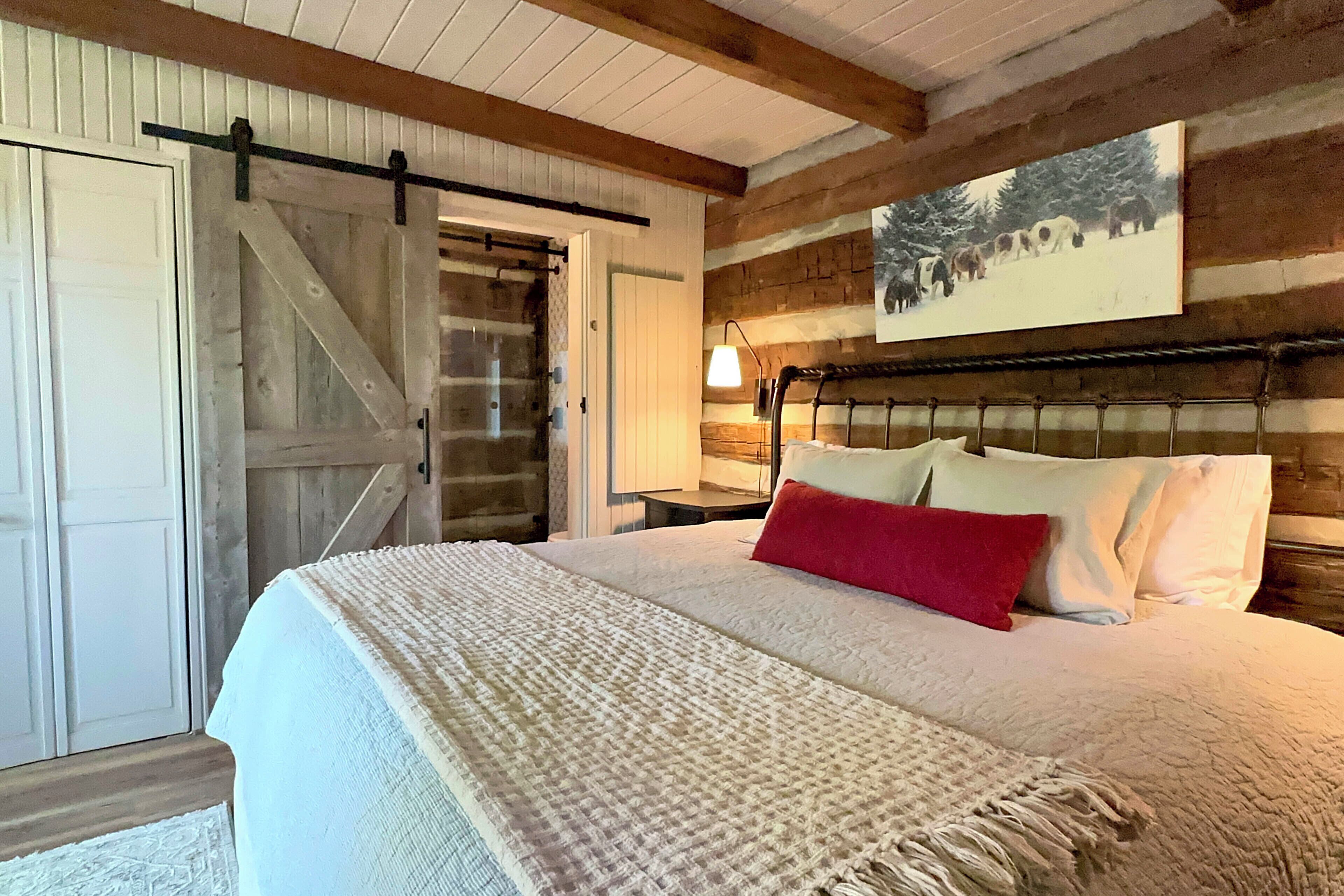 Ein Schlafzimmer mit einem Bett, einem roten Kissen, einem Holz-Kopfteil, einer weißen Tür und einem Bild an der Wand.
